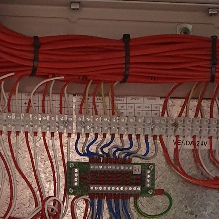 Bundled red fire cabling tied neatly into a loom above a terminal strip